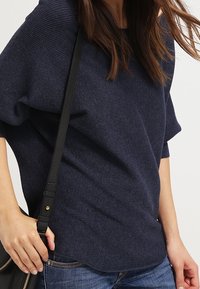 Top a coste di un blu navy con una vestibilità rilassata, scollo ampio, maniche corte e superficie testurizzata. Abbinato a jeans in denim e una borsa nera.