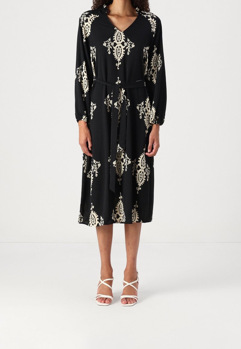 Vestido negro de manga larga y escote en V, con un patrón floral en color crema. Incluye un cinturón a juego y llega hasta la rodilla.