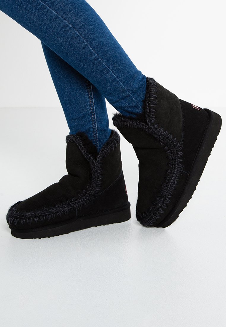 Stivaletti neri in suede con fodera in pelliccia, dotati di una cucitura decorativa lungo i bordi e una suola piatta in gomma. Indossati con jeans blu.