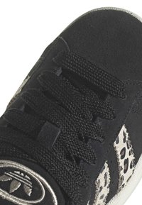 Basket en suède noir avec des accents en imprimé léopard, lacets texturés et un patch logo circulaire sur le côté. Semelle en caoutchouc visible.