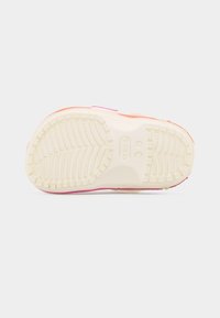 Semelle d'une chaussure pour enfants avec une adhérence texturée, motifs de bande de roulement circulaires, et logo Crocs visible en couleur blanc cassé.