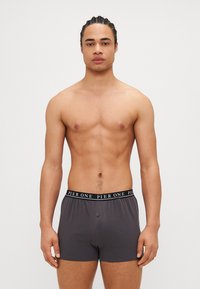 Graue Boxershorts mit einem breiteren schwarzen Bund, der mit der Aufschrift "PIER ONE" versehen ist, glatter Stoffstruktur und einer Knopfdetaillierung vorne.