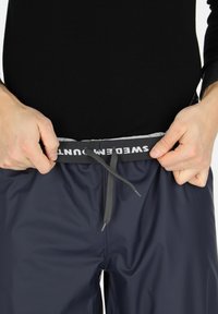 Mørkeblå vandtætte shorts med elastisk talje, der har en grå snor. Taljen har "SWEDEMMOUNT" trykt i hvid.