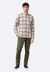 Camisa de cuadros en tonos beige, verde y azul, combinada con pantalones verde oliva y zapatillas oscuras con cordones naranjas.