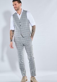 Grauer karierter Anzug mit Weste und schmal geschnittenen Hosen. Weiße Hemd darunter, hellbraune Schuhe. Merkmale sind eine maßgeschneiderte Passform und eine glatte Textur.