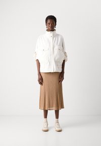 White oversized jacket with two front pockets, paired with a ribbed beige midi skirt, cream sneakers, and ankle socks. Simple design and textures.