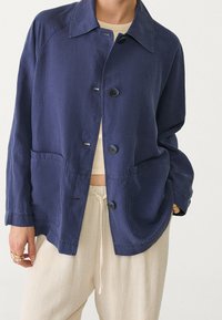 Marineblauwe jas gemaakt van lichtgewicht stof, met een kraag, knopen aan de voorkant en twee grote zijzakken.