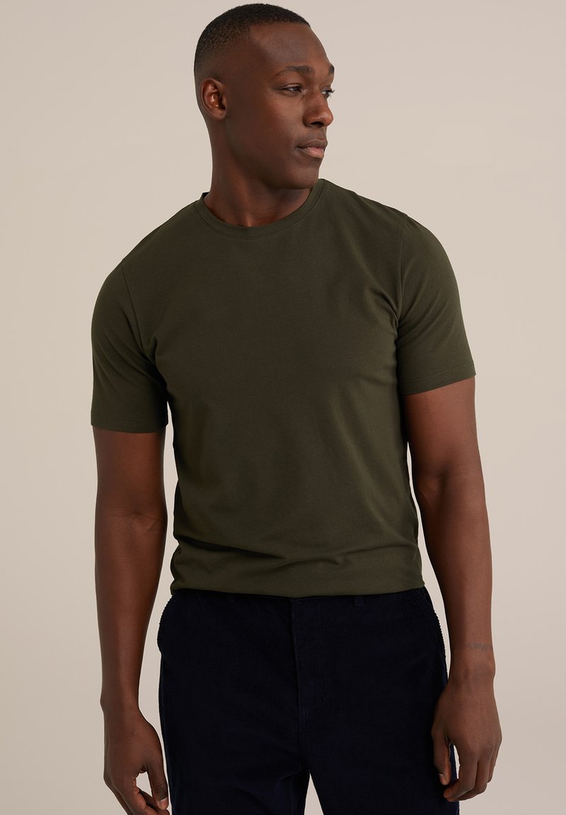 Olivově zelené tričko s krátkým rukávem vyrobené z jemné tkaniny, s klasickým kulatým výstřihem a přiléhavým střihem. Nosí se s tmavými kalhotami.