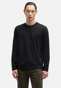 Czarna koszula z długim rękawem z bawełny z okrągłym dekoltem i dopasowanym krojem, zestawiona z oliwkowozielonymi spodniami. Gładka faktura, minimalne zdobienia.