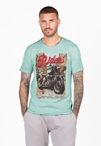 T-shirt verde menta a maniche corte con grafica di una moto vintage, testo "Riders" e "Build & Service" in rosso e bianco. Texture morbida.