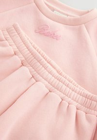 Jasnoróżowy sweter z zebranym materiałem na dole oraz haftowanym logo "Baker" w dopasowanym różowym odcieniu. Miękka tekstura.