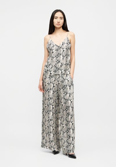 Νεαρή γυναίκα στέκεται φορώντας μαύρο και λευκό τοπ με λεπτές τιράντες και μοτίβο φιδιού, καθώς και παντελόνι φαρδύ με το ίδιο μοτίβο, συνδυασμένα με μαύρα μυτερά τακούνια.