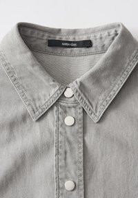 Gray denim shirt featuring a classic collar, two round silver buttons, and tonal stitching. Label reads "someday." Textured fabric.