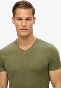 T-shirt verde oliva a maniche corte con scollatura a V, realizzato in cotone testurizzato, con un logo ricamato in modo discreto sul petto.