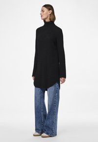 Schwarzer Rollkragenpullover mit langen Ärmeln, strukturierter Stoff, Seitenschlitze, kombiniert mit lockeren blauen Jeans und beigen Slippern.