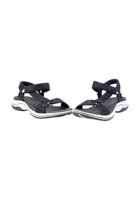 Sandalias negras con tiras entrecruzadas, que cuentan con una plantilla texturizada y un acento blanco a lo largo de la suela. Ligeras, con una suela de goma flexible.