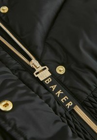 Crna jakna s valovitim uzorkom s zlatnim patentnim zatvaračem i detaljima, s istaknutom oznakom brenda "BAKER" u krupnim slovima.