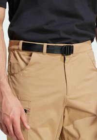 Beige cargo pants with a smooth texture, featuring a front zip pocket and black buckle belt. Worn with a dark shirt, showing a casual style.