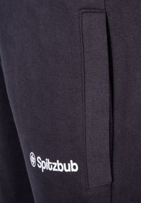 Pantalones de chándal gris oscuro hechos de una tela suave que cuentan con un bolsillo lateral, costuras planas y un logo blanco "Spitzbub" en la parte inferior de la pierna izquierda.