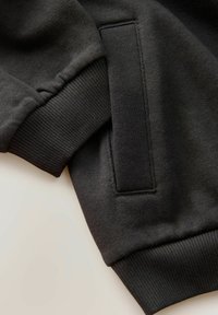 Czarna bluza z ribbowymi ściągaczami i teksturowanym korpusem. Charakteryzuje się prostym designem oraz ukrytą kieszenią z boku. Miękki materiał.