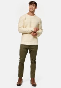 Suéter de punto textura cremosa con puños y dobladillo de canalé, combinado con pantalones ajustados en verde oliva y botas de cuero marrón hasta el tobillo.