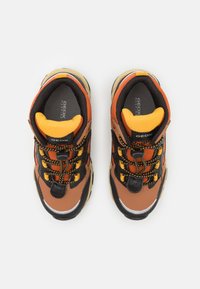 Baskets marron et orange avec des accents noirs, surface texturée et lacets noirs. Elles présentent une doublure intérieure jaune et un design géométrique.