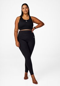 Svart sport-bh och högmidjade leggings. Båda är gjorda av mjukt, stretchigt tyg. Har en logo på både bh:n och leggingsen.