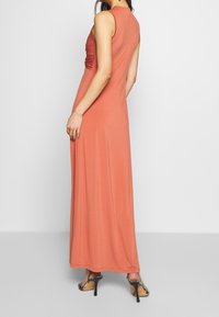 Lång, ärmlös klänning i korall, tillverkad av ett mjukt och elastiskt tyg. Har rynkade detaljer på baksidan och en golvlång design.