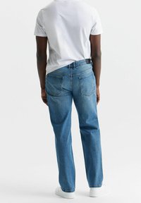 Vaqueros de mezclilla azul con un corte relajado, tira alta y dos bolsillos traseros, combinados con una camiseta blanca simple y zapatillas blancas.