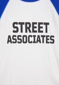 Chemise blanche avec manches bleues arborant un texte noir audacieux "STREET ASSOCIATES" centré sur le devant.