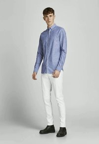 Blue button-up shirt with a collared neckline, paired with fitted white pants and black ankle boots; smooth texture and slim fit.