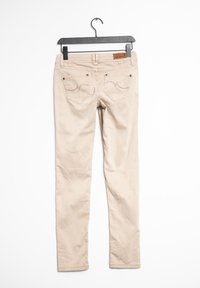 Jean skinny beige présenté sur un cintre noir. Comprend deux poches arrière avec des détails cousus et une étiquette en cuir à la ceinture.