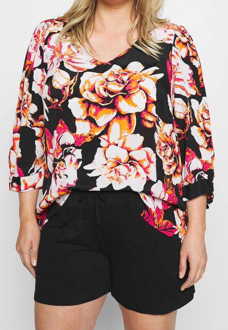 Blusa floreale con sfondo nero, caratterizzata da grandi rose bianche, rosa e arancioni; maniche a tre quarti; abbinata a pantaloni corti neri.