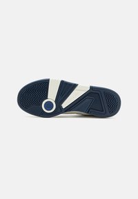 Suela de una zapatilla Lacoste blanca y azul marino, que muestra un patrón de banda de rodadura texturizado y el nombre de la marca en la media suela.