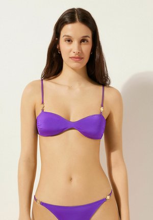 Lila bikini-set med en vadderad underwire-top med tunna axelband och dekorativt guldhardware. Slät, elastisk tygtextur.