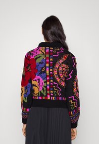 Zwarte gebreide cardigan met levendige bloemen- en geometrische patronen in rood, roze en groen, voorzien van een geribbelde zwarte kraag en manchetten.