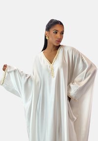 Hvid satin kaftan med V-udskæring og udsmykket guldkant langs kanterne, med brede ærmer og glat, flydende stof.