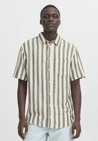 Camicia a maniche corte con righe verticali blu navy e crema, aperture con bottoni, colletto a punta e taschino sul petto. Realizzata in tessuto testurizzato.