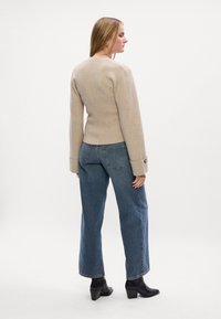 Beige strikkegenser med lange ermer, sammen med lyseblå høytaljede jeans og svarte ankelstøvler. Minimalistisk design, uten synlige mønstre.
