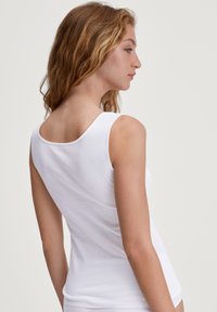 Débardeur en coton blanc avec un col rond et des bretelles de largeur moyenne, présentant une texture lisse et un design ajusté.