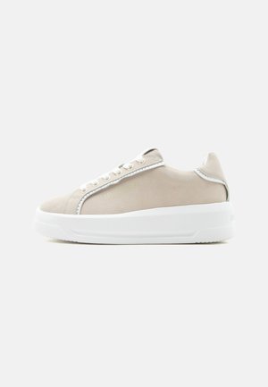 Beżowy niski sneaker z białą grubą podeszwą, białymi sznurowadłami i subtelnym srebrnym obszyciem na jednolitym jasnym tle.
