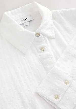 Wit overhemd met een geweven stof met kleine verhoogde stippen; voorzien van zilveren knopen en een label met de tekst "NEXT".
