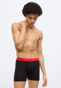 Μαύρα μποξεράκια με κόκκινη ελαστική μέση που φέρει την ένδειξη "TOMMY HILFIGER" σε λευκό κείμενο. Το ύφασμα φαίνεται λείο και ελαστικό.
