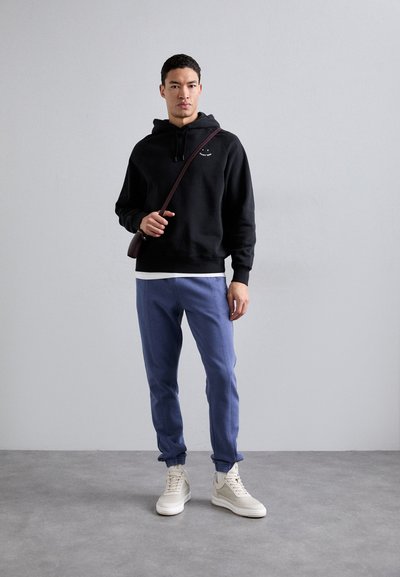 Sweatshirt preto, calças de moletom azuis, sapatilhas de cano alto em creme. Apresenta um logo no peito, capuz com cordão e uma mala tiracolo. Texturas suaves.