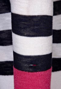Sweter z dzianiny w paski, charakteryzujący się poziomymi paskami w odcieniach granatu i bieli, z różowym mankietem. Zawiera małą metkę z logo w czerwono-biało-niebieskich akcentach.
