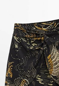 Black fabric skirt featuring golden and cream abstract patterns. Ruched design at the waist with a knot detail on the side.