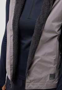 Grau-schwarwest mit einem weichen, strukturierten Innenfutter, Reißverschluss und Logopatch. Geschichtetes Design und taillierte Form mit hohem Kragen.