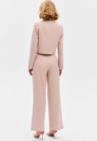 Blush roze op maat gemaakte cropped jas en wijde broek van gladde stof; met knoopaccenten op de mouwen en elegante hakken.