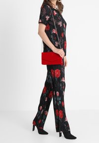 Mono negro con pliegues y patrón floral en rojo y teal, combinado con un bolso rojo y botines negros de tacón. Presenta mangas cortas y un corte relajado.