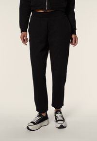 Pantalones sudaderos negros con un ajuste relajado, que cuentan con una cintura elástica, bolsillos laterales y piernas cónicas, combinados con zapatillas en blanco y negro.
